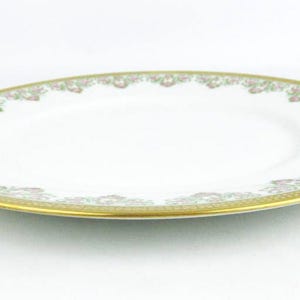 May include: Oval white porcelain plate with a gold rim and floral pattern. The plate has a wide gold band with a repeating floral design in pink and green. A classic piece for serving.