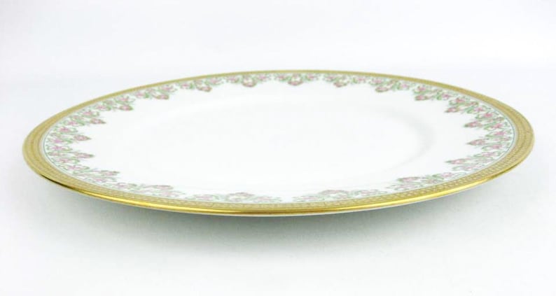 May include: Oval white porcelain plate with a gold rim and floral pattern. The plate has a wide gold band with a repeating floral design in pink and green. A classic piece for serving.