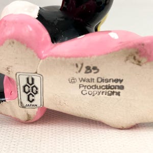 May include: A vintage ceramic Minnie Mouse figurine, featuring a pink bow and dress with white polka dots. The figurine has black ears and a black face. The bottom of the figurine has the text "&copy; Walt Disney Productions Copyright" and "UCC Japan".