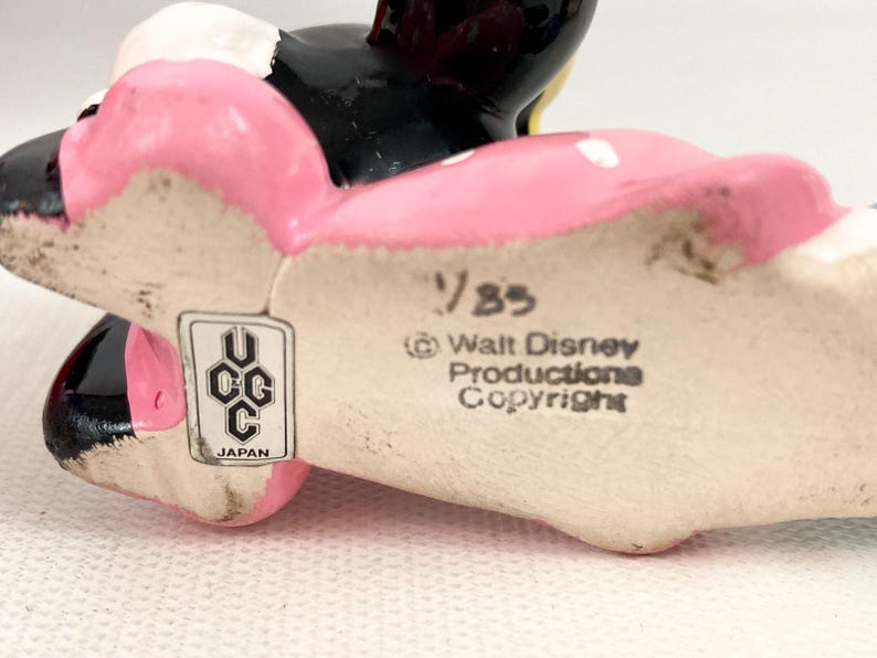 May include: A vintage ceramic Minnie Mouse figurine, featuring a pink bow and dress with white polka dots. The figurine has black ears and a black face. The bottom of the figurine has the text "&copy; Walt Disney Productions Copyright" and "UCC Japan".