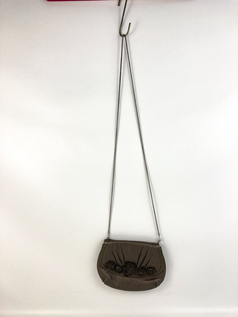 May include: A brown leather crossbody bag with a chain strap and a floral design. The bag has a flap closure and a small, rounded shape.