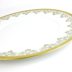 May include: Oval white serving platter with a gold rim and a floral design in pink and green. The decorative border features a repeating pattern of flowers and leaves. A classic piece for serving food.