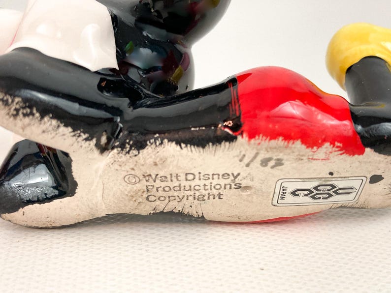 May include: A ceramic Mickey Mouse figurine, featuring black, red, white, and yellow colors. The base of the figurine has the text "Walt Disney Productions Copyright" and a "Japan" sticker.