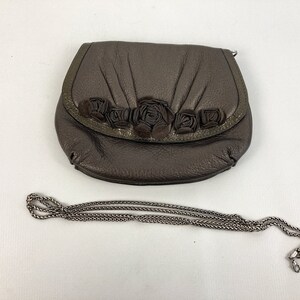 May include: A brown leather purse with a chain strap and a floral design. The purse has a flap closure and a small pocket on the front.