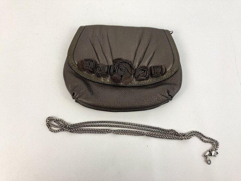 May include: A brown leather purse with a chain strap and a floral design. The purse has a flap closure and a small pocket on the front.