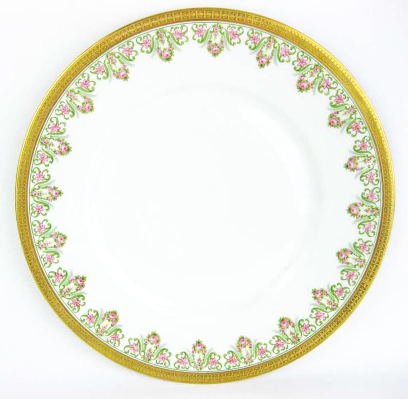 May include: White porcelain plate with a gold rim and a decorative border of pink roses and green leaves. The plate has a wide gold band with a repeating pattern. A classic piece of dinnerware.