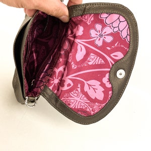 May include: A brown leather clutch purse with a floral print lining. The purse has a silver chain strap and a small metal button on the front.