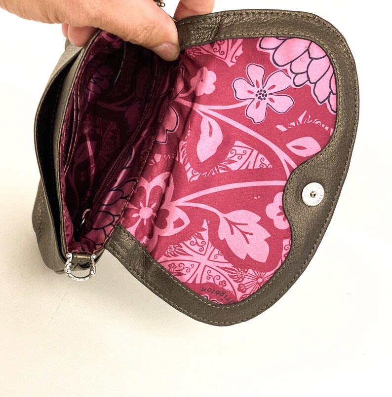 May include: A brown leather clutch purse with a floral print lining. The purse has a silver chain strap and a small metal button on the front.