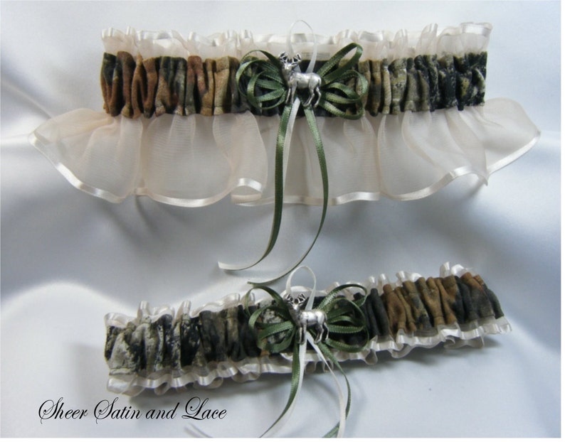 Puede incluir: Un par de ligas de novia con estampado de camuflaje, sat&eacute;n blanco y cinta verde. Las ligas tienen un dije de plata de una cabeza de venado.