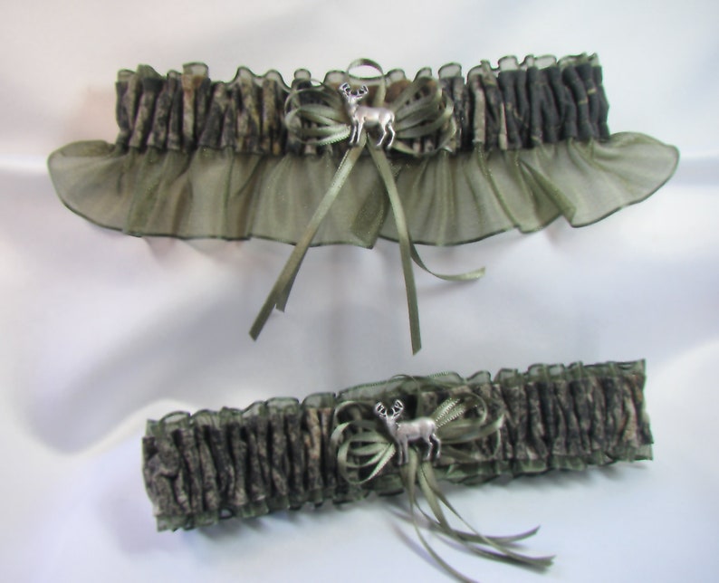 May include: A pair of green and brown camouflage garters with a silver deer charm. The garters are made of a soft, stretchy material and have a delicate lace trim.