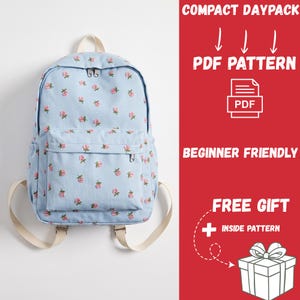 Può includere: Uno zaino azzurro con un motivo ripetuto di piccole rose rosa e foglie verdi. Lo zaino presenta una tasca frontale con cerniera, uno scomparto principale con doppia cerniera e spallacci color crema. Testo: COMPACT DAYPACK PDF PATTERN BEGINNER FRIENDLY FREE GIFT INSIDE PATTERN.