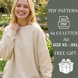 May include: A woman wearing a beige sweatshirt. The image includes text that says "PDF PATTERN", "A4 US LETTER", "Ao", "SIZE XS --3XL", and "FREE GIFT". The background is a garden with green foliage and white flowers.