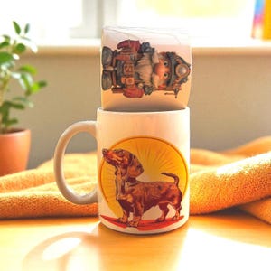 May include: Two ceramic mugs stacked on top of each other. The bottom mug features a brown dachshund dog illustration inside a yellow circle. The top mug has a cartoon image of a gnome with a beard and goggles.