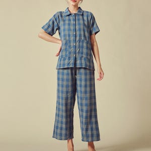 Puede incluir: Un conjunto de pijama a cuadros azul y blanco con camisa de cuello y pantalones anchos.