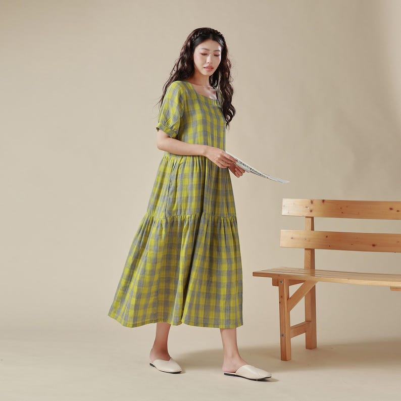 May include: A yellow and gray plaid midi dress with a square neckline and short puff sleeves. The dress has a tiered skirt and is made of a lightweight fabric.