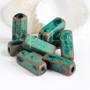 May include: A group of eight teal green and copper colored rectangular beads with a distressed finish. The beads have a hole in the center and are perfect for jewelry making.