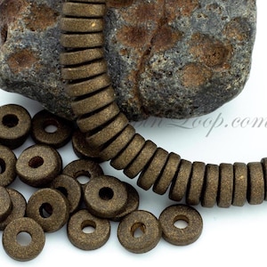 May include: A close-up of a strand of brown donut-shaped beads with a matte finish. The beads are scattered on a white surface. The beads are approximately 1/2 inch in diameter.
