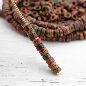 May include: A strand of brown, green, and red wooden beads with a gold bead at the end. The beads are strung on a gold wire.