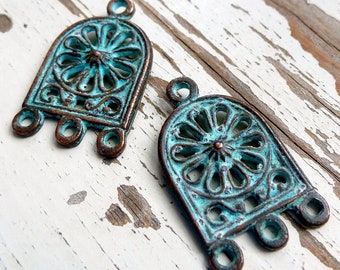 May include: Two antique-style metal pendants with a turquoise patina. Each pendant features a decorative, openwork design with a circular motif in the center. The pendants have three loops at the bottom for attaching to a chain or cord.