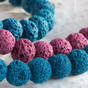 Peut inclure: Gros plan sur un collier de perles en lave volcanique bleues et roses. Les perles sont rondes et ont une texture rugueuse et poreuse.