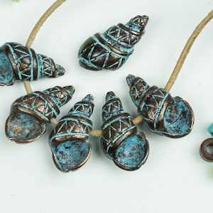 Può includere: Sei perline a forma di conchiglia di colore turchese e marrone con disegni intricati. Le perline sono infilate su un cordoncino di cuoio marrone.