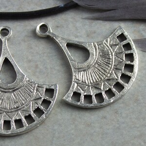 Puede incluir: Dos abalorios de metal plateado en forma de abanico con intrincados dise&ntilde;os geom&eacute;tricos. Los abalorios tienen un bucle en la parte superior para sujetarlos a joyas.