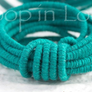May include: Teal colored cord wound into a coil with a knot in the center.