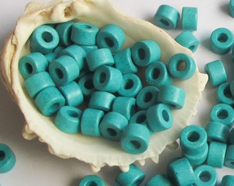 May include: A large quantity of turquoise blue ceramic beads in a seashell. The beads are round with a hole in the center.