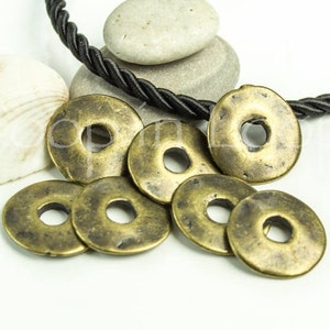 May include: A group of eight antique brass-colored metal rings with a hole in the center. The rings are arranged in a random pattern on a white surface.