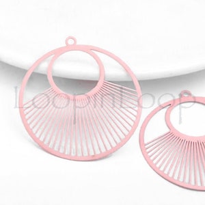 May include: Two pink metal earring blanks with a circle design and a sunburst pattern. The blanks are perfect for creating custom earrings.
