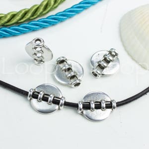 May include: Silver metal beads with a decorative design. The beads are round and have a raised pattern of lines. The beads are strung on a black cord.