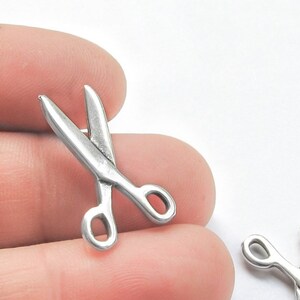 May include: Two silver-toned metal scissor charms. The charms are about 1 inch long and are perfect for adding a touch of whimsy to jewelry or crafts.