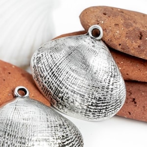 May include: Two silver clam shell charms with a textured surface and a loop for hanging.