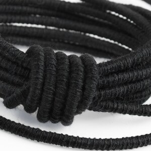 May include: A black braided bracelet with a knotted design. The bracelet is made of multiple strands of braided cord.