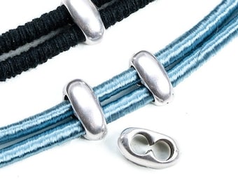 Könnte beinhalten: Silberne Metallperlen für die Schmuckherstellung. Die Perlen sind oval geformt und haben eine glatte, glänzende Oberfläche. Die Perlen sind auf zwei Strängen elastischer Schnur gezeigt, einer schwarzen und einer blauen.