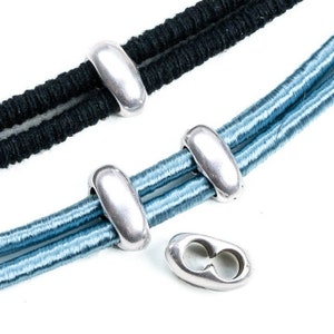 May include: Silver metal beads for jewelry making. The beads are oval shaped and have a smooth, shiny finish. The beads are shown on two strands of elastic cord, one black and one blue.