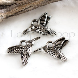 May include: Three silver hummingbird charms with a textured finish. The charms have a loop at the top for attaching to jewellery or other crafts.