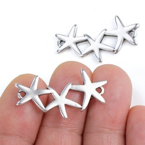 May include: Two silver-toned metal charms shaped like starfish, each with five points. The charms are connected to each other, forming a continuous chain of starfish.