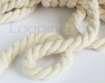 May include: A close-up of a thick, natural cream-coloured cotton rope. The rope is twisted and knotted, showing its texture and detail.