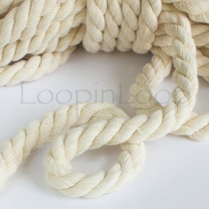 May include: A close-up of a thick, natural cream-coloured cotton rope. The rope is twisted and knotted, showing its texture and detail.