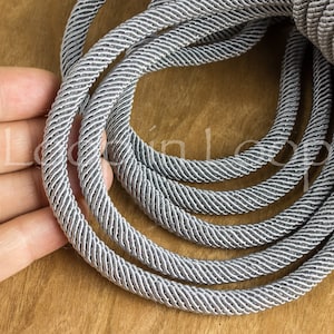Op de afbeelding: Close-up van een zilveren en grijs gevlochten koord. Het koord is gedraaid en heeft een subtiele glans.
