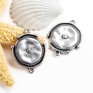 May include: Two silver-toned metal connector charms with a round, textured design and a small bead in the center. Each charm has three loops for attaching to jewelry.