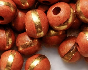 May include: A collection of round, terracotta beads with a gold stripe painted around the centre of each bead. The beads have a hole through the centre for stringing.