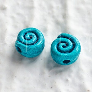 May include: Two turquoise blue ceramic beads with a spiral design. The beads have a hole in the center for stringing.
