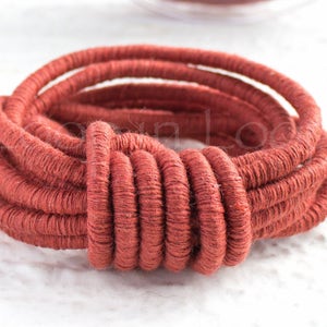 May include: Close-up of a coil of terracotta-colored rope. The rope is tightly wound, with visible texture and a slightly rough appearance. The coil is centered, with a blurred background.