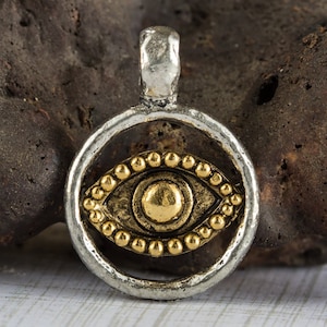 May include: Silver pendant with a gold evil eye charm. The eye is surrounded by a circle of small gold beads.