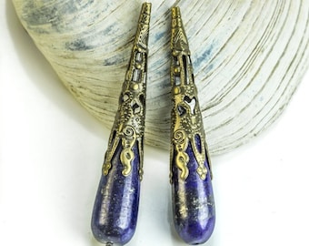 Pode incluir: Um par de brincos de pedra lazuli em forma de lágrima com detalhes em metal dourado. Os brincos têm um design detalhado e ornamentado.