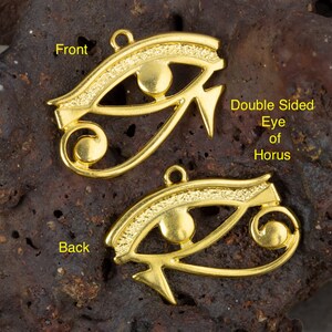 May include: Double-sided gold-tone Eye of Horus pendant charm. The front features a detailed eye design with a raised circle in the center. The back features a similar design with a raised circle at the bottom.