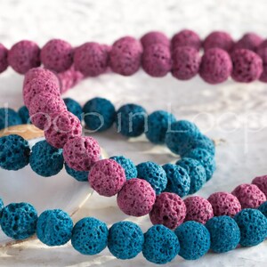 May include: Two strands of lava rock beads, one strand is pink and the other is blue. The beads are round and have a rough, textured surface.