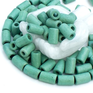 Puede incluir: Una gran cantidad de cuentas de cerámica verde con un agujero en el centro de cada cuenta. Las cuentas están dispuestas en círculo sobre una superficie blanca.